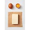 Top view of butter block on paper with raw chicken eggs over white background