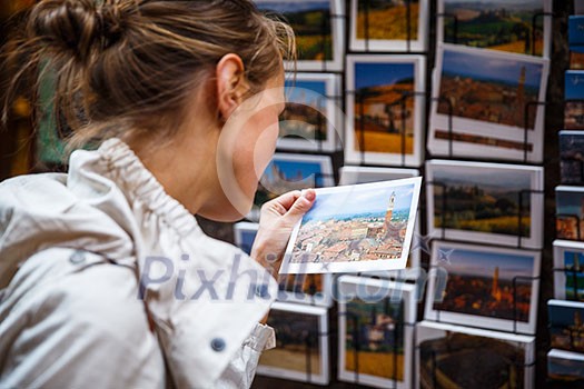 Young woman choosing the right postcard to send home from a vacation abroad (shallow DOF; color toned image)