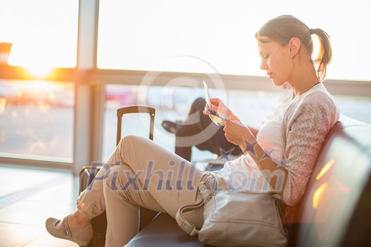 Young female passenger at the airport, waiting for her flight lit by warm evening light, about to board her flight, checking her boarding pass (shallow DOF; color toned image)