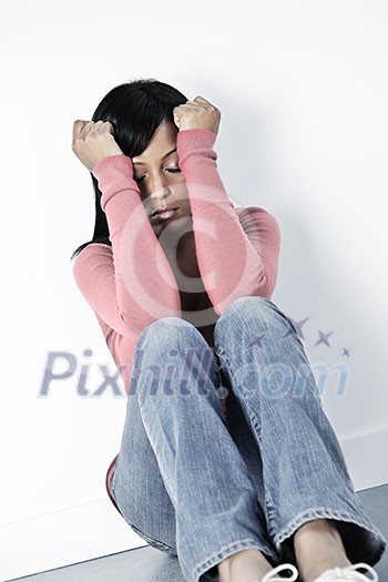 Depressed black woman sitting against wall on floor with eyes closed