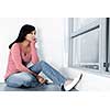 Depressed black woman sitting against wall on floor looking out window