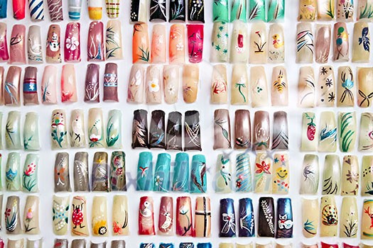 Artificial acrylic nails painted in various designs on display in nail salon
