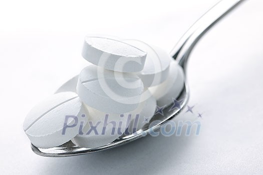 Calcium supplement pills piled on metal spoon closeup