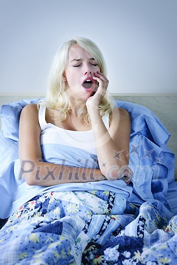 Sleepy blonde woman yawning sitting up in bed
