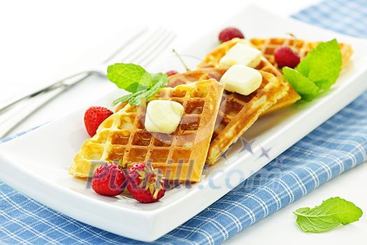 Plate of belgian waffles with fresh strawberries and pats of butter