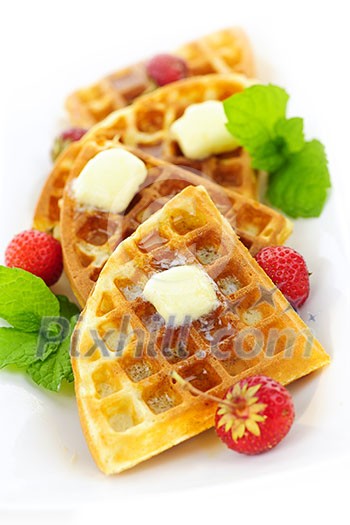 Plate of belgian waffles with fresh strawberries and pats of butter