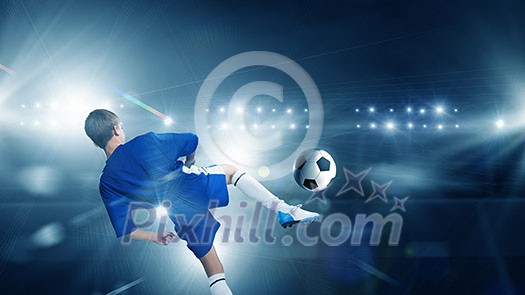 Rear view of kid boy in blue uniform on soccer stadium kicking ball