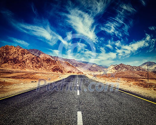 Vintage retro effect filtered hipster style image of road in mountains Himalayas and dramatic clouds on blue sky. Ladakh, Jammu and Kashmir, India