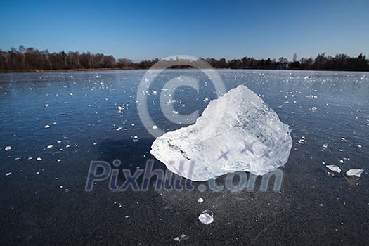 Freezing winter temperatures: block of ice lying on the surface of a frozen pond on a sunny winter day