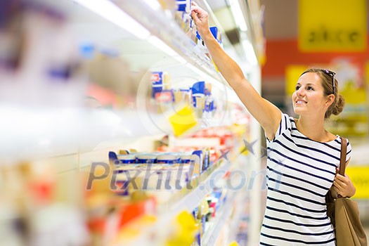 Beautiful young woman shopping for diary products at a grocery store/supermarket (color toned image)