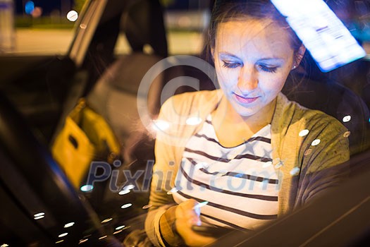 Pretty young woman using her smart phone while driving her car at night