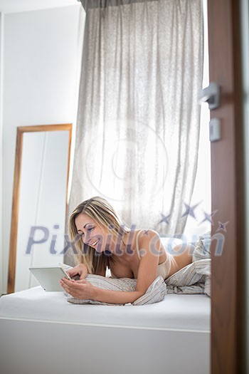 Beautiful young woman in bed, using her tablet computer first thing in the morning