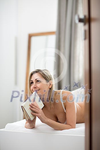 Beautiful young woman in bed, reading her favorite book (shallow DOF, color toned image)