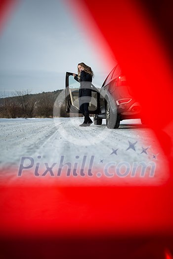 Young woman setting up a warning triangle and calling for assistance after her car broke down in the middle of nowhere on a freezing winter day Young woman setting up a warning triangle and calling for assistance after her car broke down in the middle of nowhere on a freezing winter day