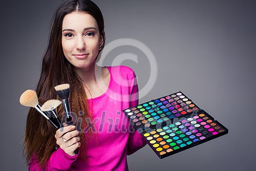 Cute make-up artist holding her vast palette of colors and hands with brushes around her (color toned image) Cute make-up artist holding her vast palette of colors and hands with brushes around her (color toned image)