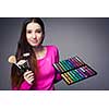 Cute make-up artist holding her vast palette of colors and hands with brushes around her (color toned image)