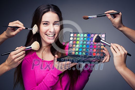 Cute make-up artist holding her vast palette of colors and hands with brushes around her (color toned image) Cute make-up artist holding her vast palette of colors and hands with brushes around her (color toned image)