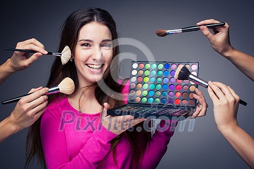 Cute make-up artist holding her vast palette of colors and hands with brushes around her (color toned image)