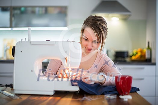 Beautiful young woman sewing clothes with sewing machine (color toned image; shallow DOF)