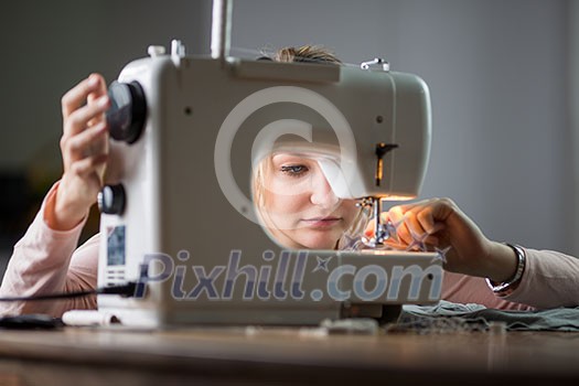 Beautiful young woman sewing clothes with sewing machine (color toned image; shallow DOF)