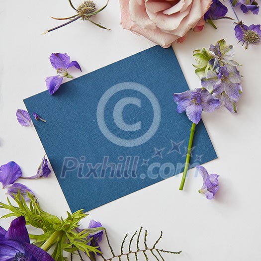 Frame of spring flowers with a blue piece of paper under the text, flat lay