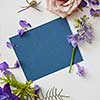 Frame of spring flowers with a blue piece of paper under the text, flat lay