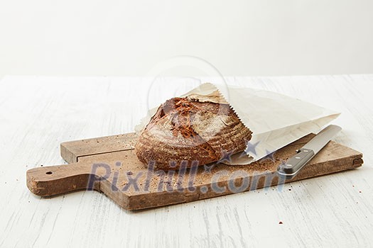 Homemade bread wrapped in paper on a wooden board with a knife on a light background Homemade bread wrapped in paper on a wooden board with a knife on a light background
