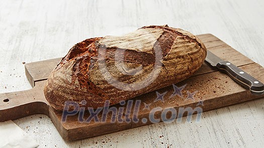 Rye oval bread on a cutting board with a knife on a white background