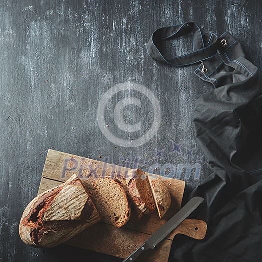 Concept of baking and cooking background. Sliced dark bread. Bread with a knife on a wooden board on a dark background