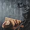 Concept of baking and cooking background. Sliced dark bread. Bread with a knife on a wooden board on a dark background