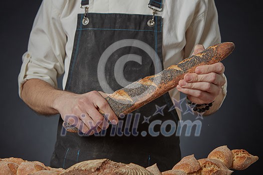 Men's hands holding a fresh baguette with poppy seeds on a dark background clous up Men's hands holding a fresh baguette with poppy seeds on a dark background clous up