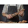 Men's hands holding a fresh baguette with poppy seeds on a dark background clous up