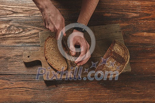 Baker cuts freshly baked organic bread on a wooden brown background flat lay Baker cuts freshly baked organic bread on a wooden brown background flat lay