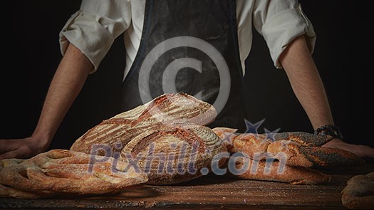 Baker with fresh bread on wooden brown table background Baker with fresh bread on wooden brown table background