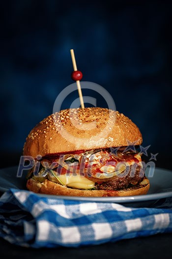 Close Up of Fresh Burger on Dark Rustic Wooden Surface with Blue Background.