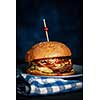 Close Up of Fresh Burger on Dark Rustic Wooden Surface with Blue Background.