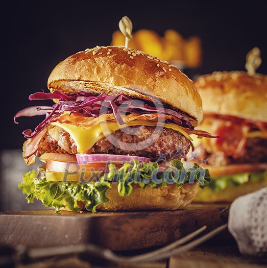 Delicious fresh burger with meat, bacon, cheese and vegetables on a wooden board, in a rustic soul style. Retro vintage toned image.