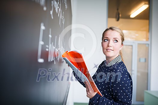 Pretty, young college student writing on the chalkboard/blackboard during a math class