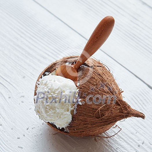 Homemade organic coconut ice cream. An ice cream ball in a wooden spoon in coconut Close up on a white wooden background Homemade organic coconut ice cream. An ice cream ball in a wooden spoon in coconut Close up on a white wooden background