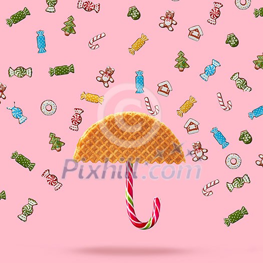 Umbrella made of waffle and Christmas candy on a pink background.