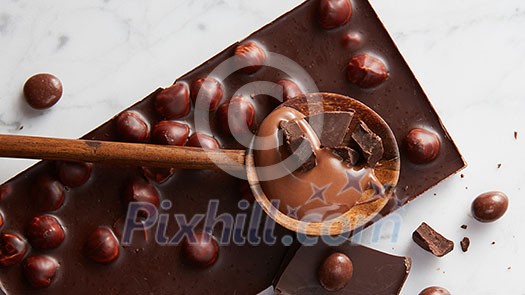 wooden spoon with chocolate and chocolate balls on a white marble background