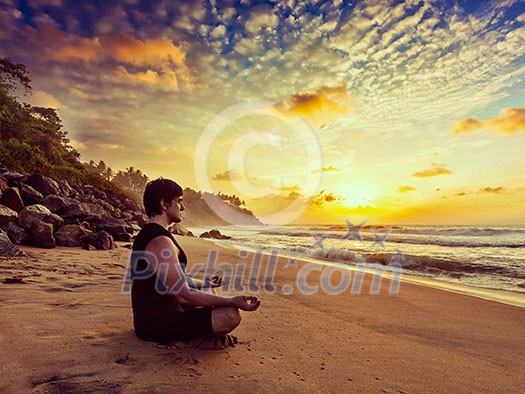 Vintage retro effect hipster style image of sporty fit man doing yoga meditating in padmasana lotus pose on tropical beach on sunset Vintage retro effect hipster style image of sporty fit man doing yoga meditating in padmasana lotus pose on tropical beach on sunset