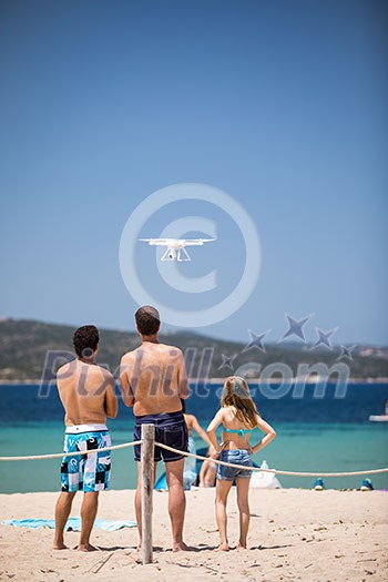 Young people flying a drone by remote control on a beach/sea shore, enjoying summer vacation. Young people flying a drone by remote control on a beach/sea shore, enjoying summer vacation.