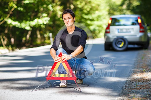 Handsome young man with his car broken down by the roadside, setting the safety triangle Handsome young man with his car broken down by the roadside, setting the safety triangle