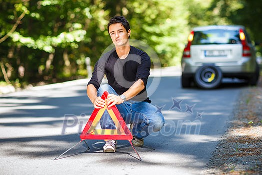 Handsome young man with his car broken down by the roadside, setting the safety triangle