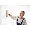 Senior man painting a wall in with paint roller, smiling, enjoying the work