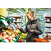 Beautiful, young woman shopping for fruits and vegetables in produce department of a grocery store/supermarket (shallow DOF; color toned image)