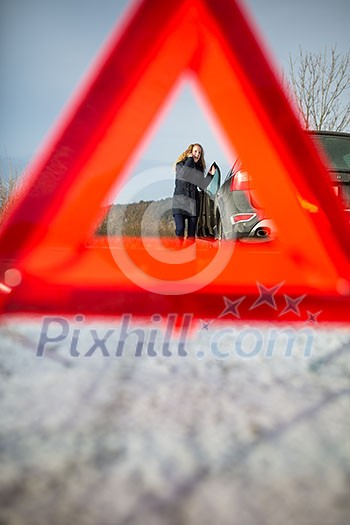 Realy angry young woman in a road distress situation - setting up a warning triangle and calling for assistance after her car broke down in the middle of nowhere on a freezing winter day