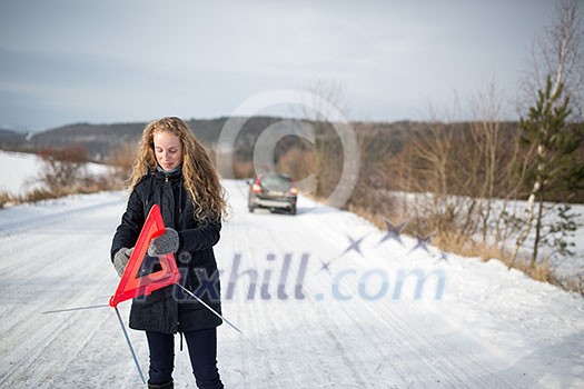 Young woman setting up a warning triangle and calling for assistance after her car broke down in the middle of nowhere on a freezing winter day Young woman setting up a warning triangle and calling for assistance after her car broke down in the middle of nowhere on a freezing winter day