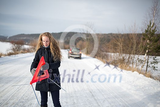 Young woman setting up a warning triangle and calling for assistance after her car broke down in the middle of nowhere on a freezing winter day